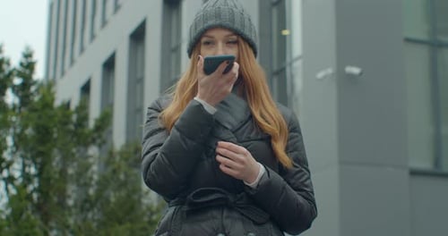 Young Redhead Woman with Long Hair Writes a Voice Message on Her Smartphone. Street Talk