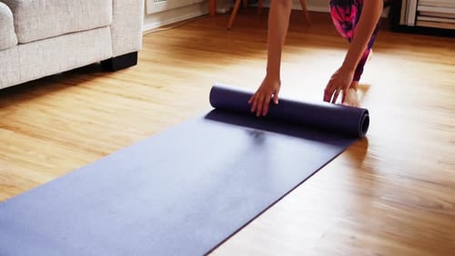Beautiful woman unrolling exercise mat on wooden floor