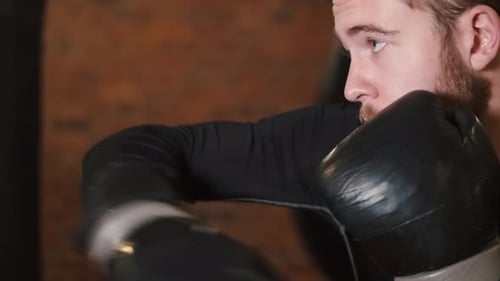 Dedicated Young Man Punching Boxing Bag at Gym