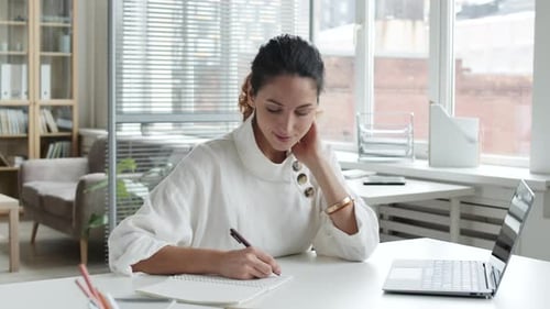 Woman Writing in Notebook at Office Desk