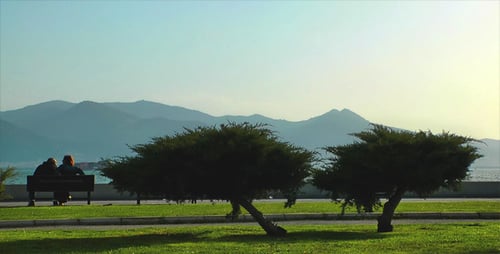 Couple Sits on Bench Overlooking Ocean and Mountains