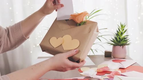 Hands Placing Card in a Gift Decorated with Hearts