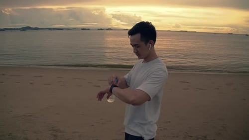Young Adult Checking Smartwatch on Beach at Sunset