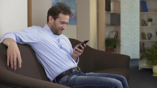 Geografielehrer sitzt auf dem Sofa und scrollt auf dem Smartphone, Technologien