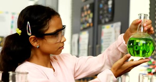 Girl Examines Flask of Green Liquid in Classroom