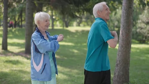 Medium Shot Fit Senior Couple Warming Up Exercising Simultaneously in Sunny Park Outdoors