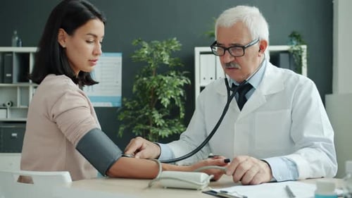 Doctor Checking Blood Pressure and Pulse Examining Female Patient in Hospital