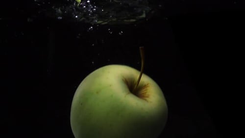 Zeitlupenaufnahme: Grüner Apfel fällt und schwimmt im Wasser. Schwarzer Hintergrund. Video zum Thema Essen Apple