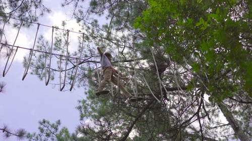 A Young Man in an Adventure Park. He Wears a Safety Harness. He Climbs on a High Rope Trail. Outdoor