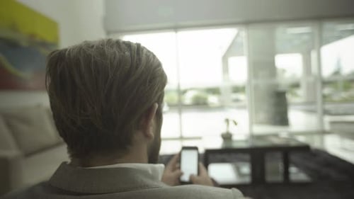 Man Using Mobile Phone in Bright Modern Living Room