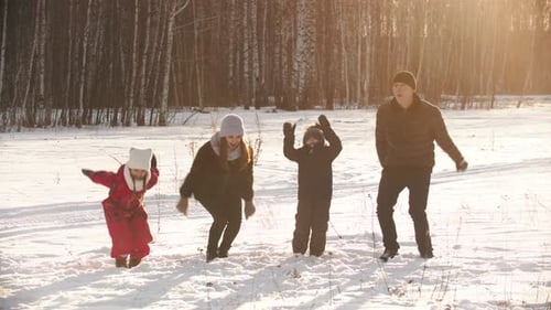 A Happy Family Holding Hands and Jumping Near the Winter Forest on Sunset