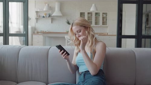 Woman Using Smartphone and Smiling on Sofa