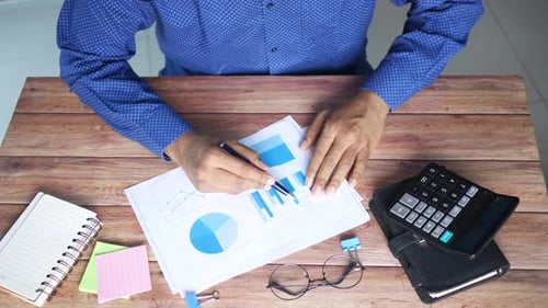 Vista superior da mão do homem com caneta analisando o gráfico de barras no papel