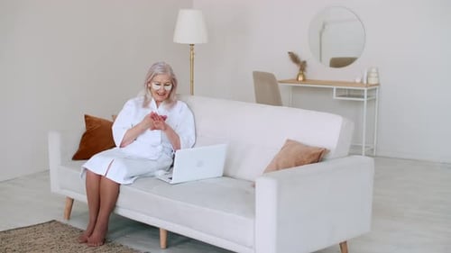 Senior Woman Applying Lotion and Using Laptop