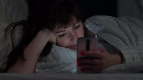 Brunette Pretty Woman Lies on the Bed and Uses the Phone at Night