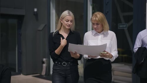 Businesswomen Discussing Documents Outside Office Building