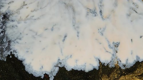 La peinture blanche s'étale sur un fond noir et doré en mouvement