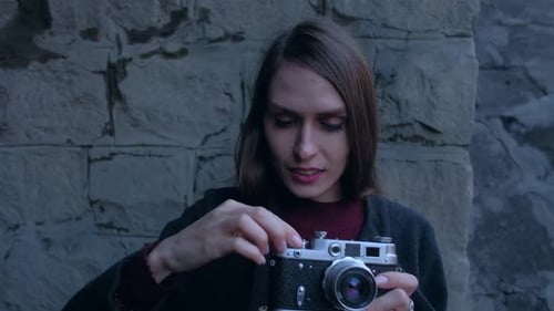 Woman Adjusts Antique Camera Outdoors Against Brick Wall
