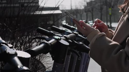 Woman Using Phone Next to Row of Scooters