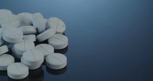 Round White Pills Accumulating on Reflective Blue Surface