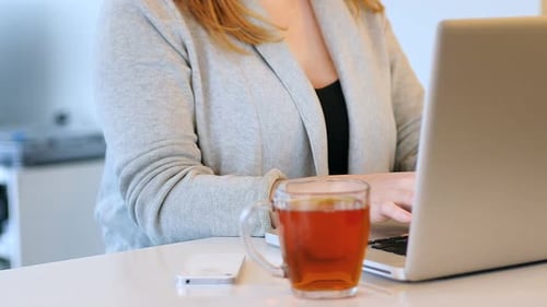 Woman Working on Laptop with Cup of Tea