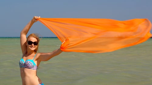 Woman Holds Orange Scarf on Beach in Bikini