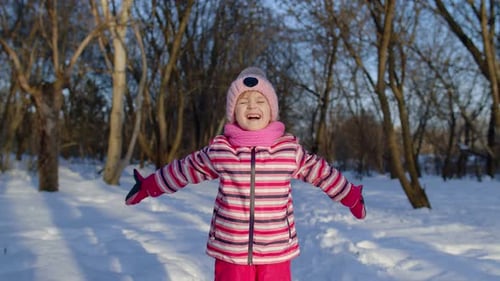 Fröhliches kleines Kind Mädchen wirft Schnee hoch lächelnd Spielen zeigt Daumen hoch im Winter Park Forest