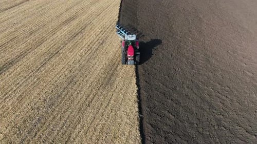 Tractor pulls a plow across a farm field. preparation of the field before sowing. Drone view.
