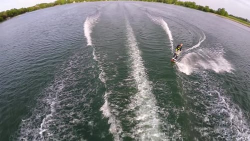 Aerial birds-eye drone view of a man wakeboarding behind a boat.