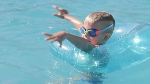 Little Boy in Swimming Pool Child Having Fun Sitting on Blue Swimming Ring Playing Under Water