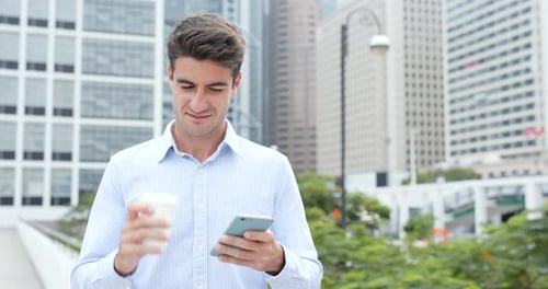 Man Using Smartphone and Drinking Coffee in City