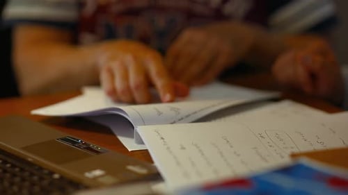 Person Studying at Desk with Notes and Laptop