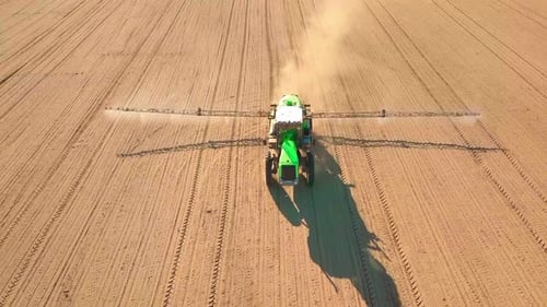Tractor Spraying a Field with Sprayer Herbicides and Pesticides at Sunset
