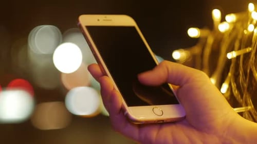 Hand Using Smartphone at Night with City Lights