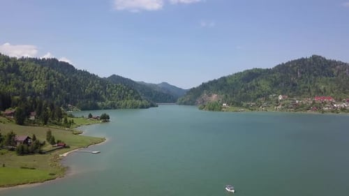 Aerial lowering shot of lake front with small boat in the foreground and valley in the background