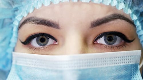 Nahaufnahme einer Ärztin, die eine OP-Maske trägt und in die Kamera blickt