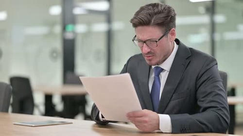 Serious Middle Aged Businessman Doing Paperwork in Office