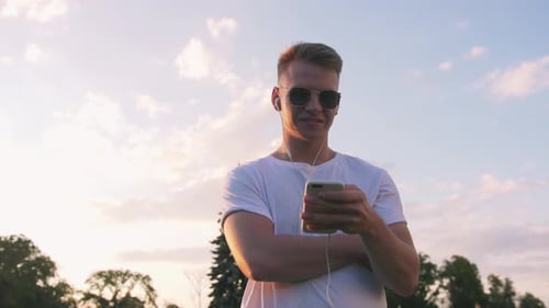 Handsome Young Hipster Man Using Smartphone Outdoors in Park