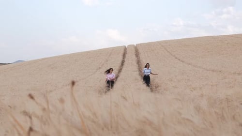Two young female friends enjoying the nature together while walking in a wheat field.