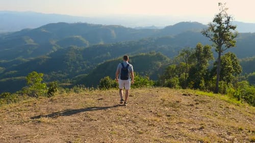 Back View of Traveler Backpacker Man Walking on Hill with Green Mountain Valley View