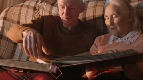 Una pareja de ancianos está considerando un álbum de fotos familiar envuelto en una tela escocesa