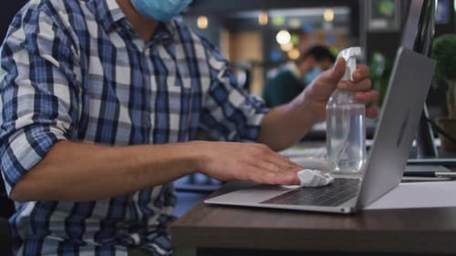 Man Sanitizing Laptop in Modern Office Setting