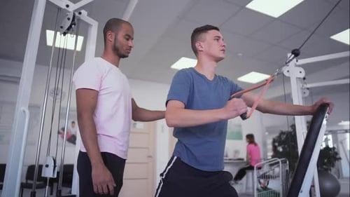 African-american Coach Helps Young Guy To Train. People in the Gym
