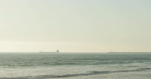 Buque de carga navegando en un océano brumoso con olas que llegan a la orilla de la playa en Figueira da Foz, Portugal