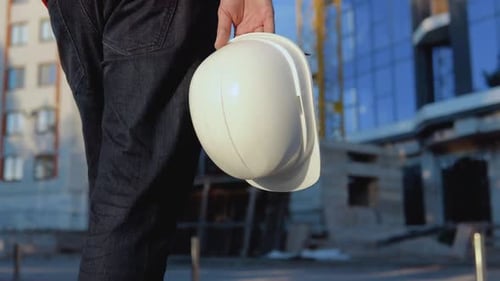 Un ingénieur-architecte vêtu d'une chemise blanche et d'un gilet de travail orange se tient debout sur fond de décor moderne