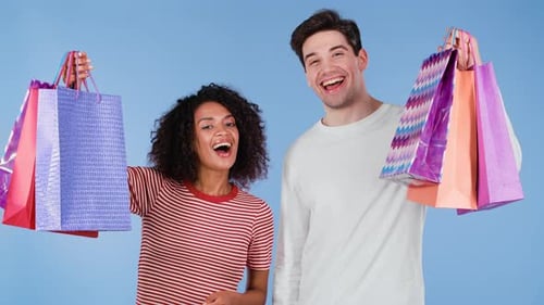 Interracial Shopaholic Couple Holds Shopping Paper Bags on Blue Studio Background