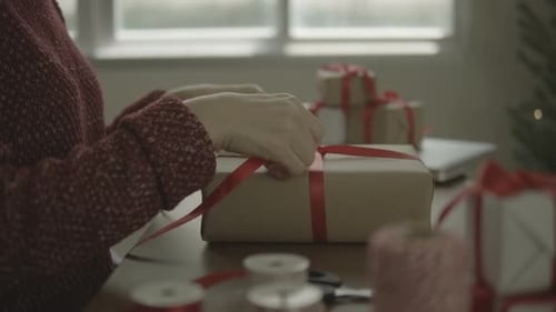 Woman Tying Red Ribbon Around Christmas Present