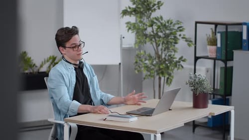 Young Adult in Headset Teleconferencing at Office Desk
