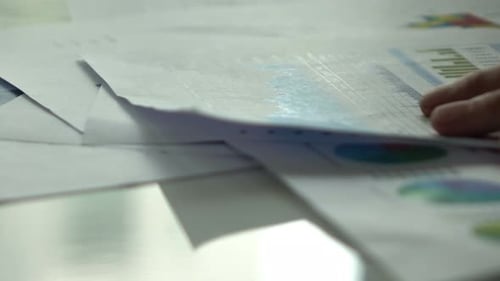 Hand Flips Through Financial Documents and Charts