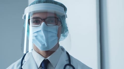 Studio portrait of young professional medical doctor in mask, hat and protective visor.